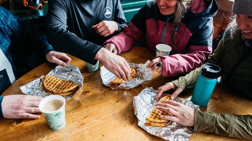 Group of skiers with waffles and coffee on a table.