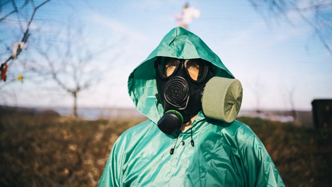 a doomsday prepper in black gas mask and green protective raincoat outdoors in spring