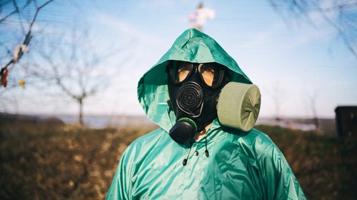 a doomsday prepper in black gas mask and green protective raincoat outdoors in spring