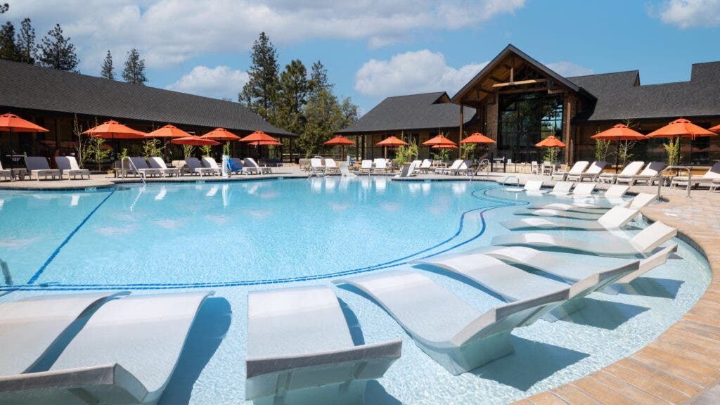 The new Firefall Ranch west of Yosemite National Park has a large outdoor pool with lounge chairs and tables with orange umbrellas.