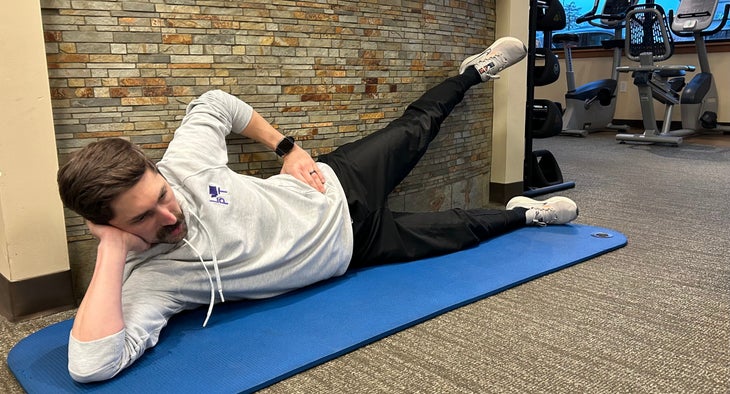 Man lies on side with one leg up in the air resting on a wall behind him