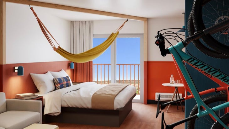 A rendition of a king room at the upcoming LOGE hotel in St. Gear, Utah, shows a bed with a hammock strung above it, a mountain bike mounted on the opposite wall, and a balcony with views over the desert. 