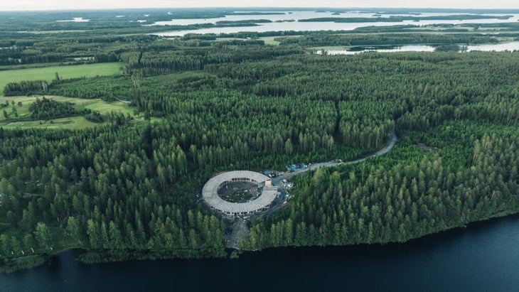 An aerial view of the O-shaped Kotona Manor hotel amid a landscape of trees and lakes in Finland