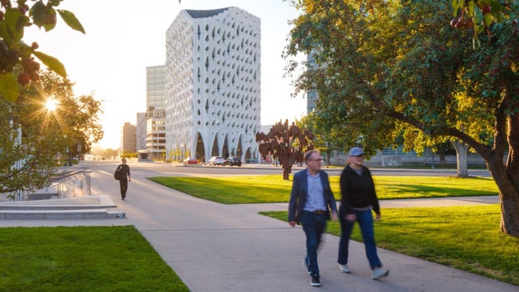 Two men walk in Denver's green Civic Center Park; behind them is the white facade of the Populus hotel