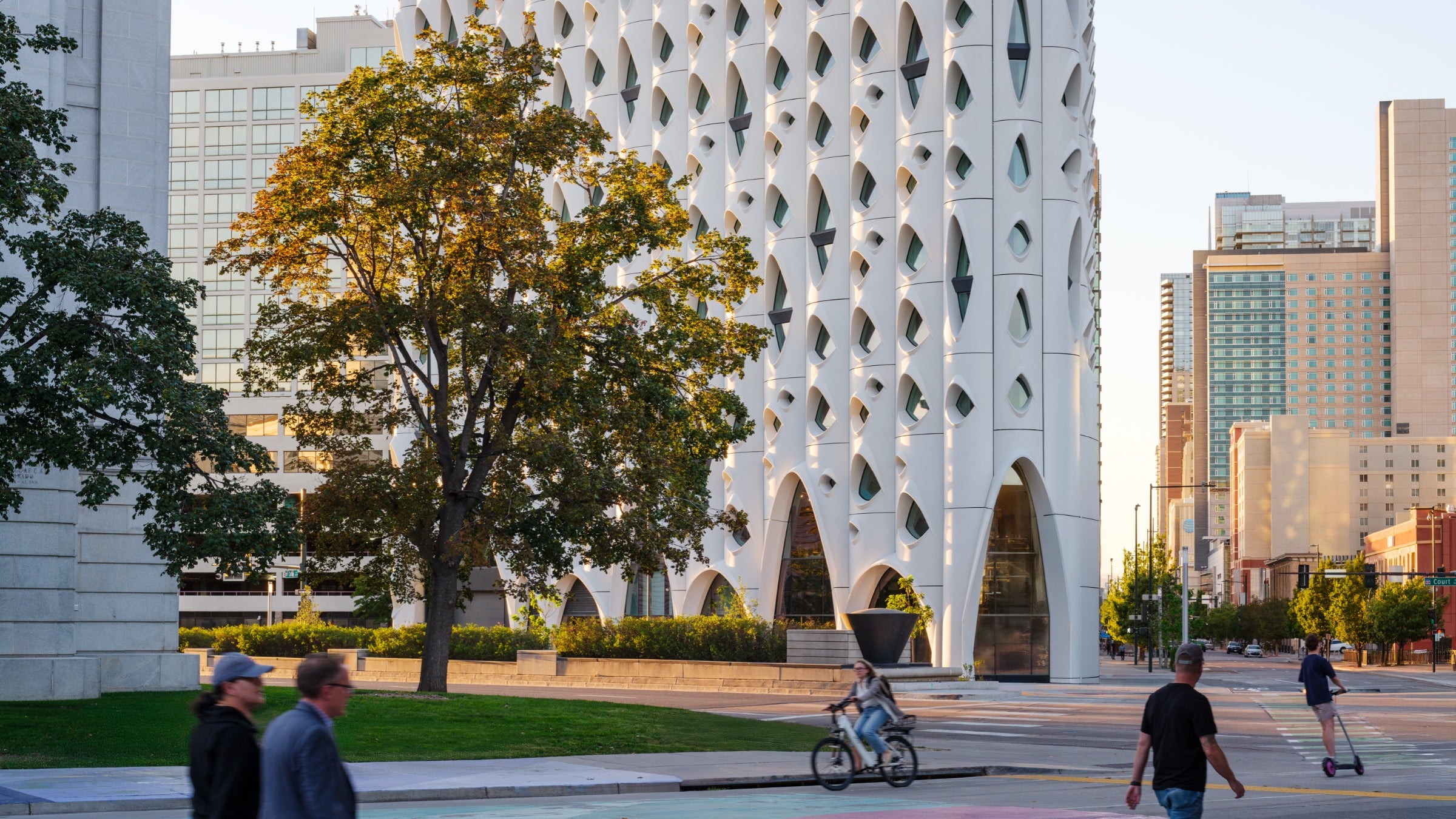 The Populus hotel, which is white and was designed to resemble a grove of aspens. A few people walk across a plaza adjacent to the building.