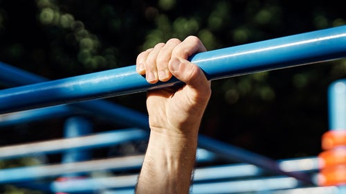 Close-up view of a man's hand gripping a gymnastic bar while doing a pull-up in a public park.