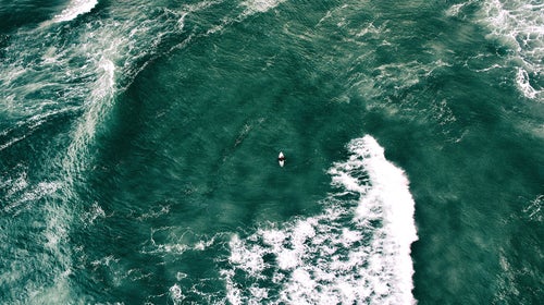 A tiny surfer sitting on surfboard in the midst of the great sea
