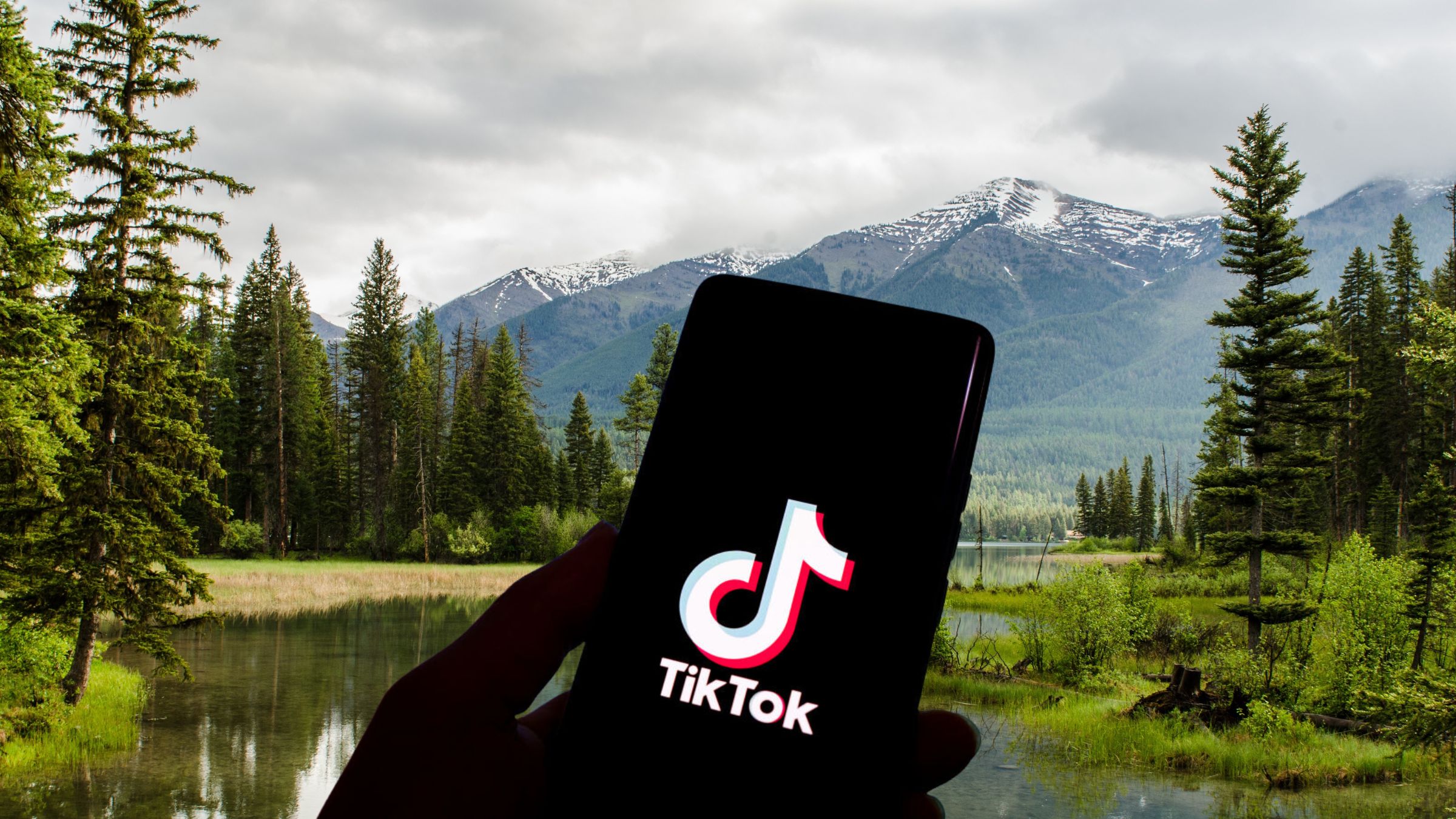 TikTok logo on phone screen against mountain background