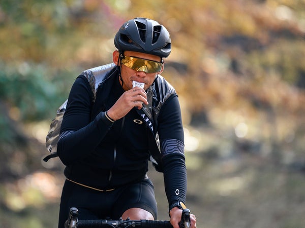 A triathlete riding a pike consumes a sport nutrition product, which is likely an ultra-processed food. A nutritionist weighs in on what that means for athletes.