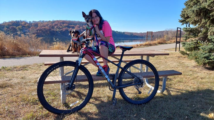 woman posing with two dogs and bike