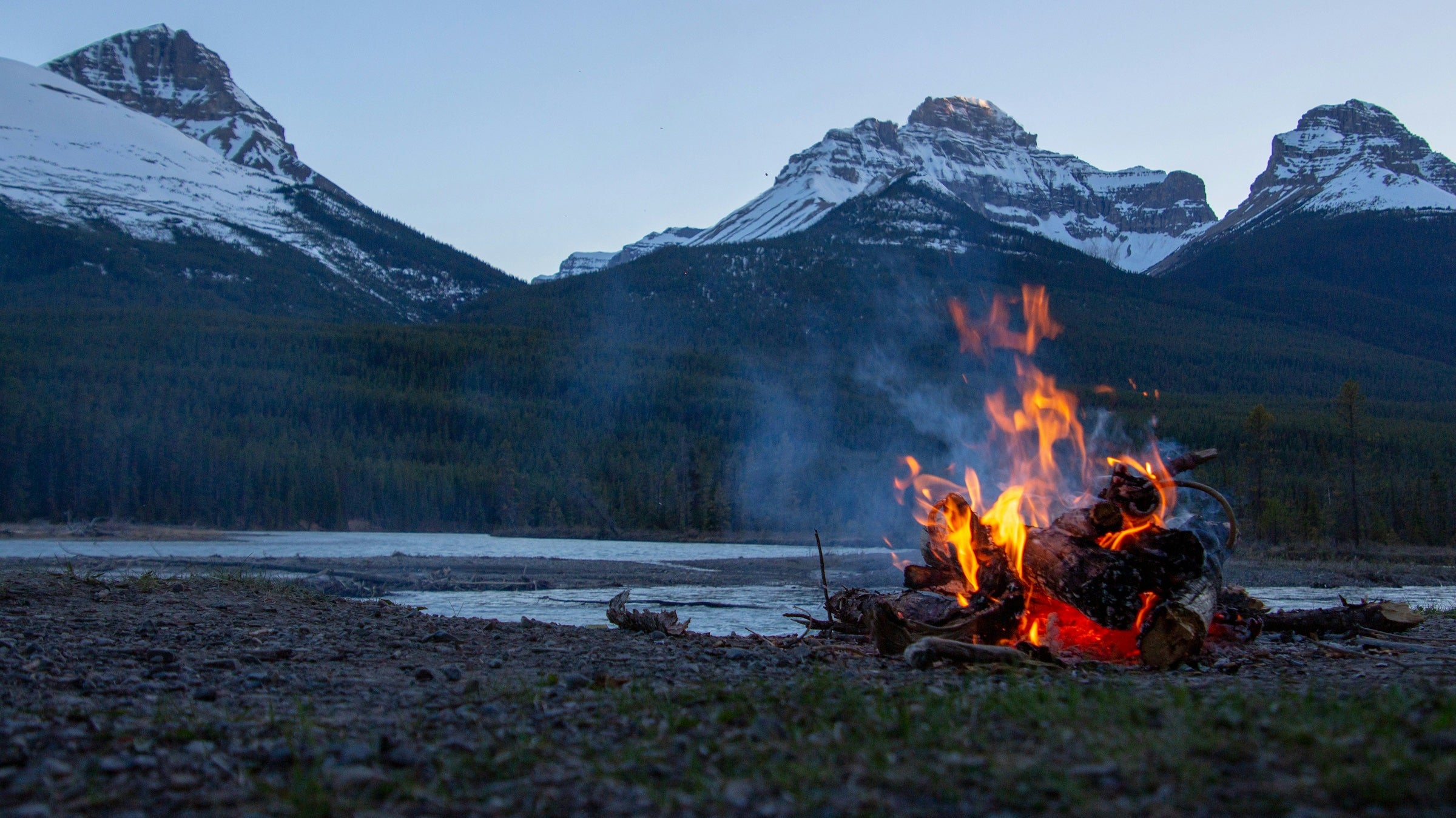 campfire in front of river and snowy mountains