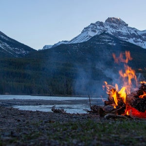 campfire in front of river and snowy mountains