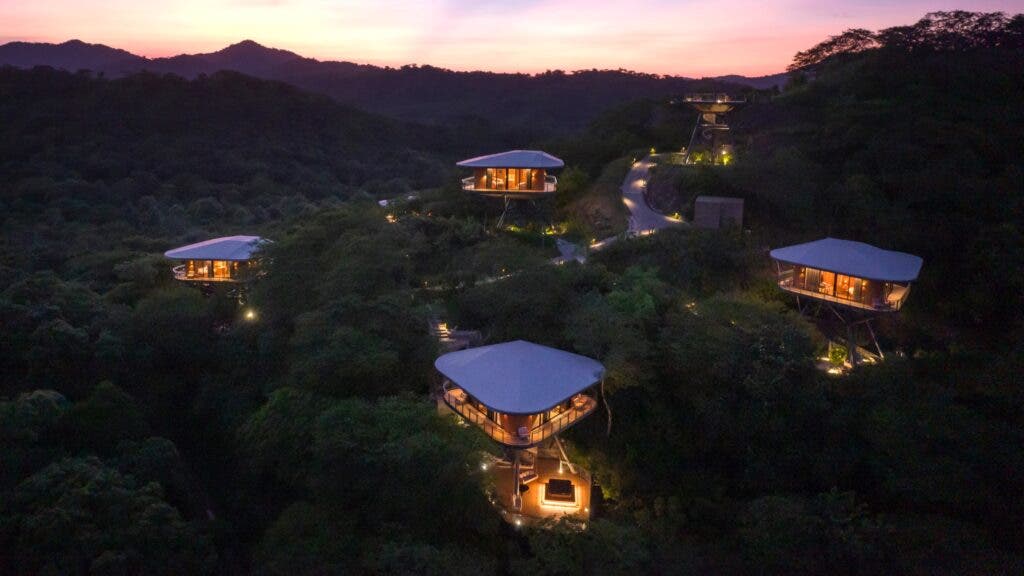 An aerial view of Suitree Experience Hotel’s treehouse bungalows perched amid the rolling hills of Costa Rica's interior at dusk.