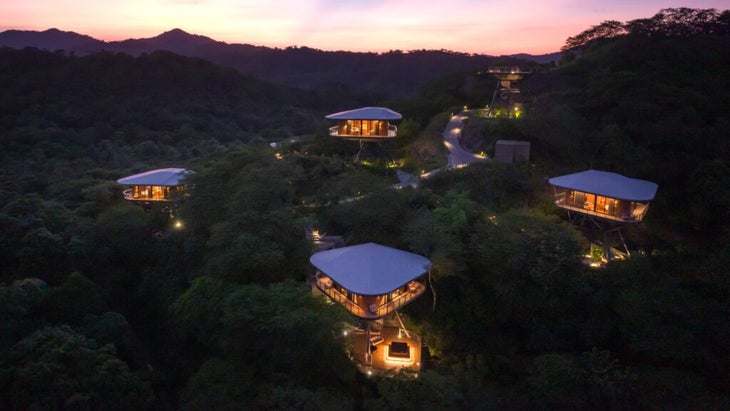 An aerial view of Suitree Experience Hotel’s treehouse bungalows perched amid the rolling hills of Costa Rica's interior at dusk.