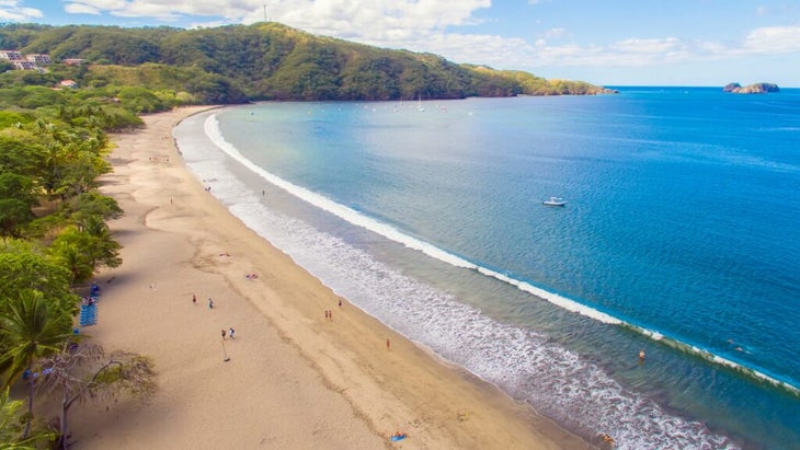 An aerial view of Costa Rica’s calm Playa Hermosa, on the Pacific coast, with people swimming and beach-going.