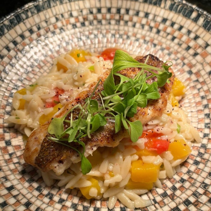 A plated dish of risotto with vegetables, topped b a grilled fish with greens, from the Suitree Experience Hotel in Costa Rica