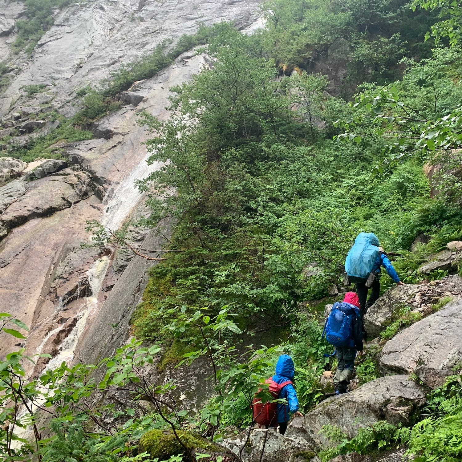 three hikers scrambling up next to waterfall