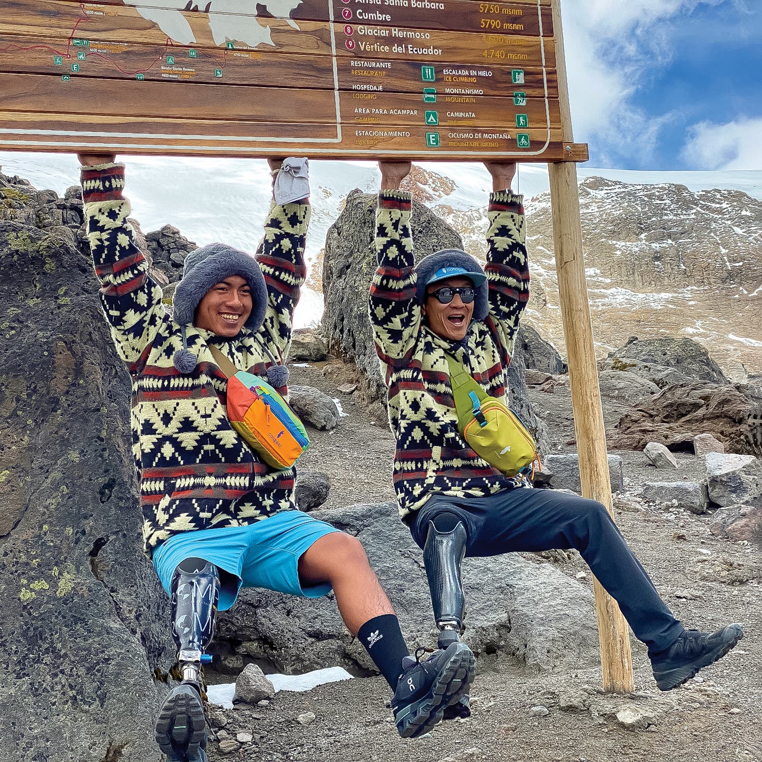 Aguinda and Lin hanging from the sign at Cayambe base camp.
