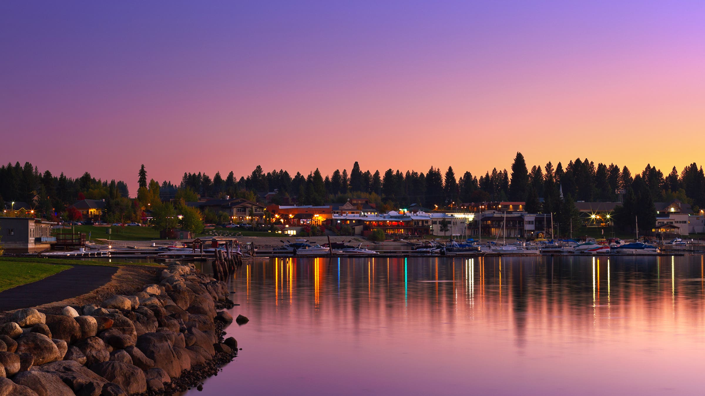 The sparkling lights of the small adventure town of McCall, Idaho, reflect across the calm waters of Payette Lake at sunset