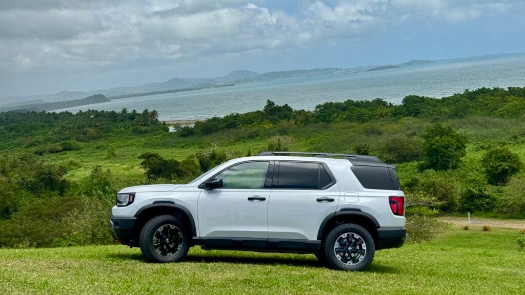 a white 2026 Honda Trailsport Passport parked on a grassy incline with a view of the coast behind it