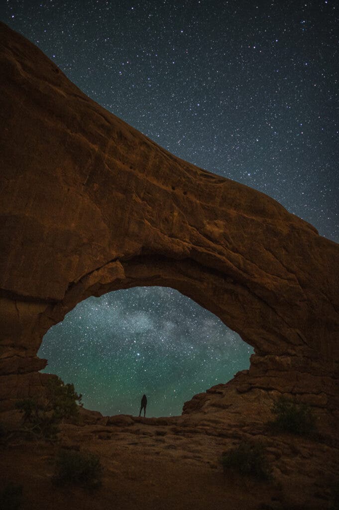 a person standing under an arch with the milky way