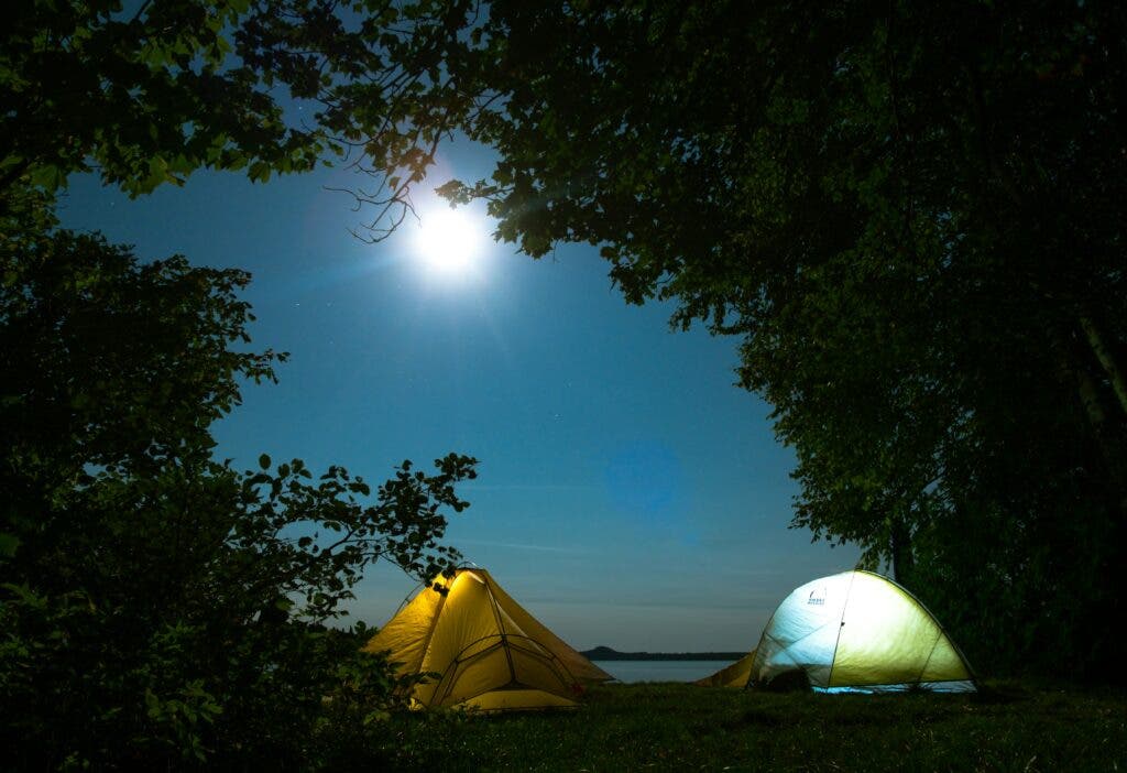 two tents lit by a bright moon in the forest at night