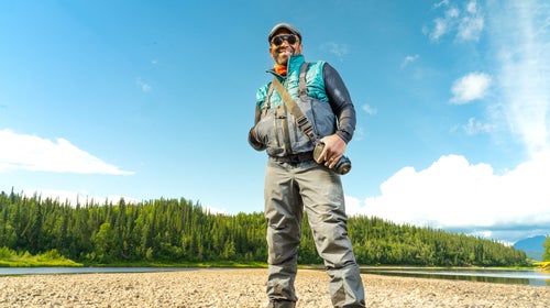 James Edward Mills in a national park wearing fishing gear and smiling under a blue sky