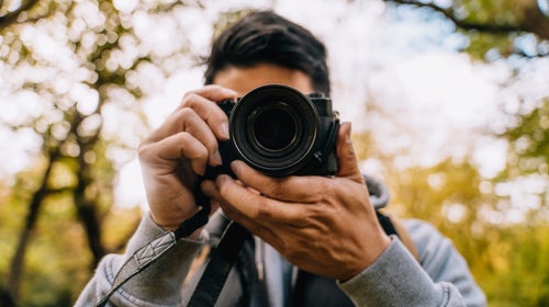 Closeup of young photographer hiking in forest and photographing nature.