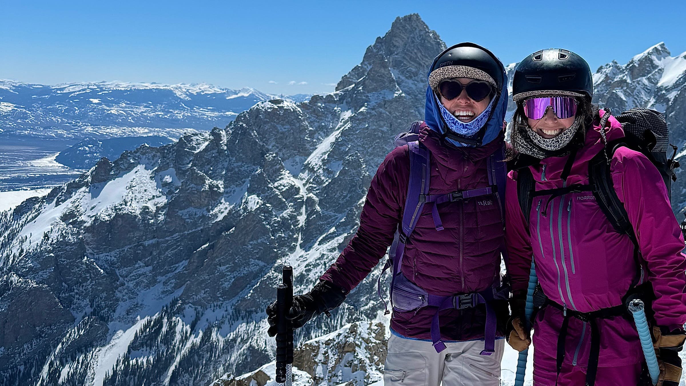 Two skiers posing in front of mountain peaks with snow