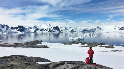 two people in antarctica wearing red and looking at icebergs
