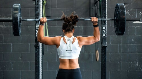 A woman lifting a large barbell over her head in an overhead press