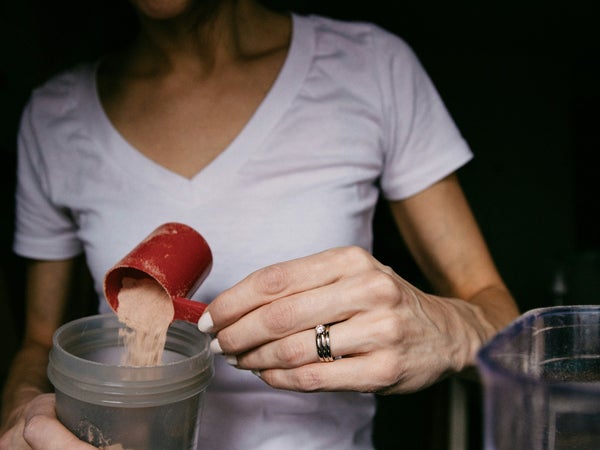 A woman pours protein powder into a protein shaker bottle