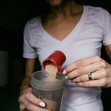 A woman pours protein powder into a protein shaker bottle