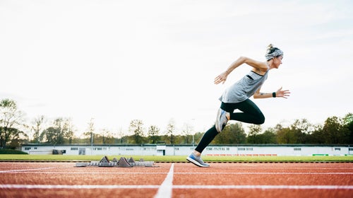 A woman wearing sports clothing sprinting off the starting blocks on an outdoor running track.