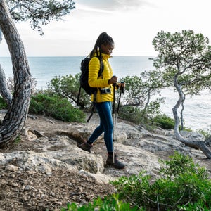 A woman in a yellow jacket hikes along the coast with trekking poles