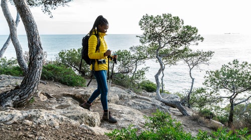 A woman in a yellow jacket hikes along the mediterranean coast