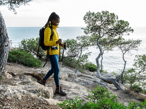 A woman in a yellow jacket hikes along the mediterranean coast