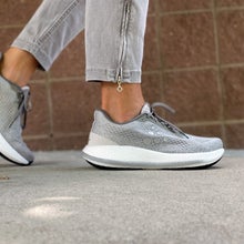 woman's feet in gray running shoes walking on pavement in front of brick wall