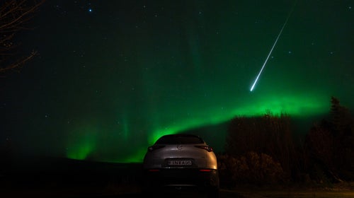 fireball streaking across green night sky over car