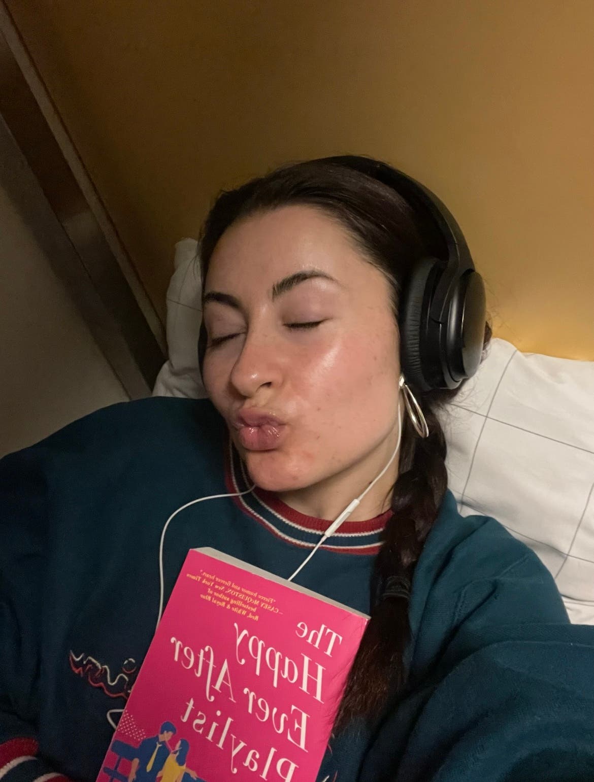 a person wearing headphones while laying in bed and holding a pink book
