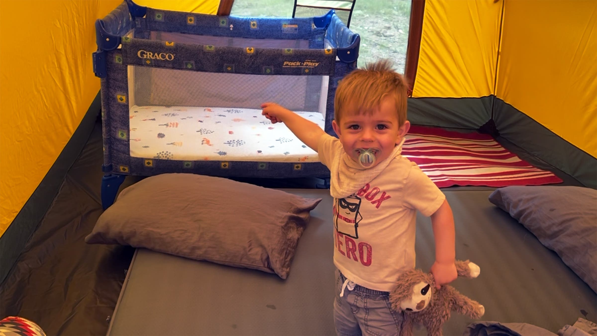 Little boy inside tent pointing to pack-n-play in tent