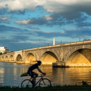 A bicyclist rides during sunset along the Mt. Vernon Trail that follows the Potomac River in Virginia near the Arlington Memorial Bridge, the Lincoln Memorial and Washington Monument seen in the background,