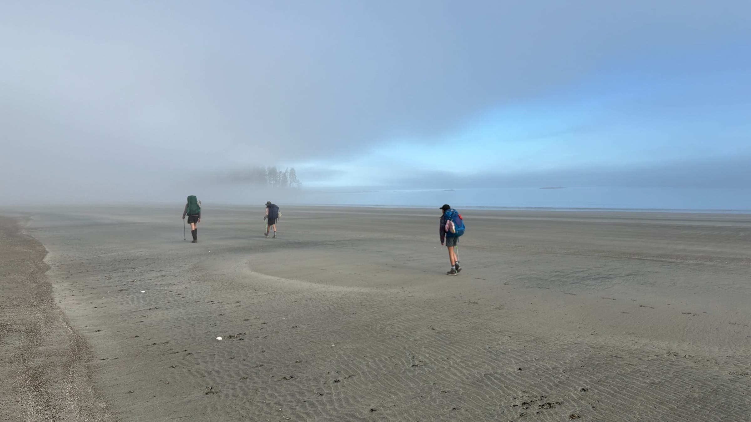 three hikers on very remote, foggy beach