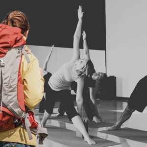 A woman wearing a red backpack observes a yoga class