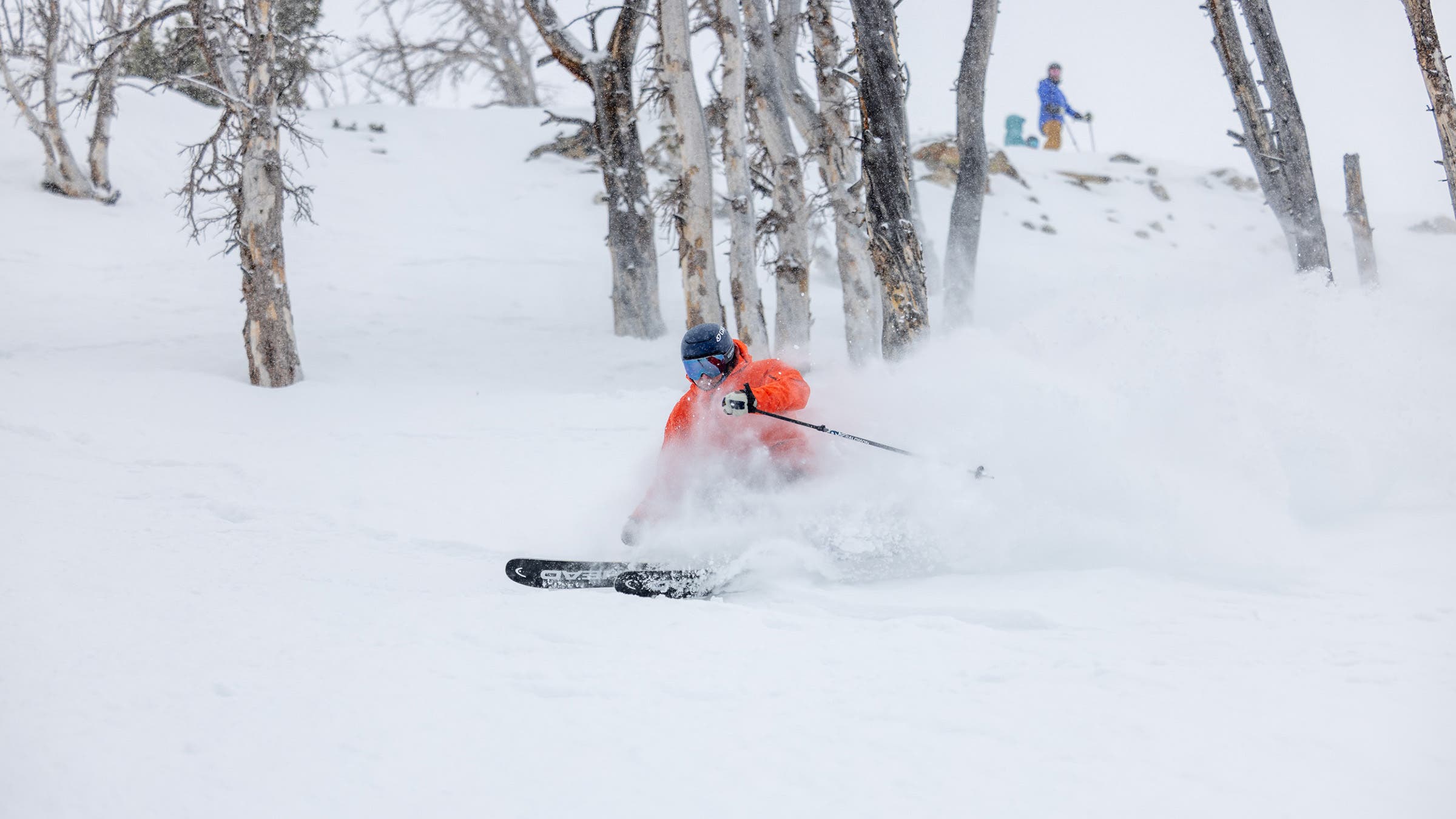 Skier in orange jacket skiing in powder snow on Head Kore 100 Ti all-mountain skis at SKI Test at Big Sky