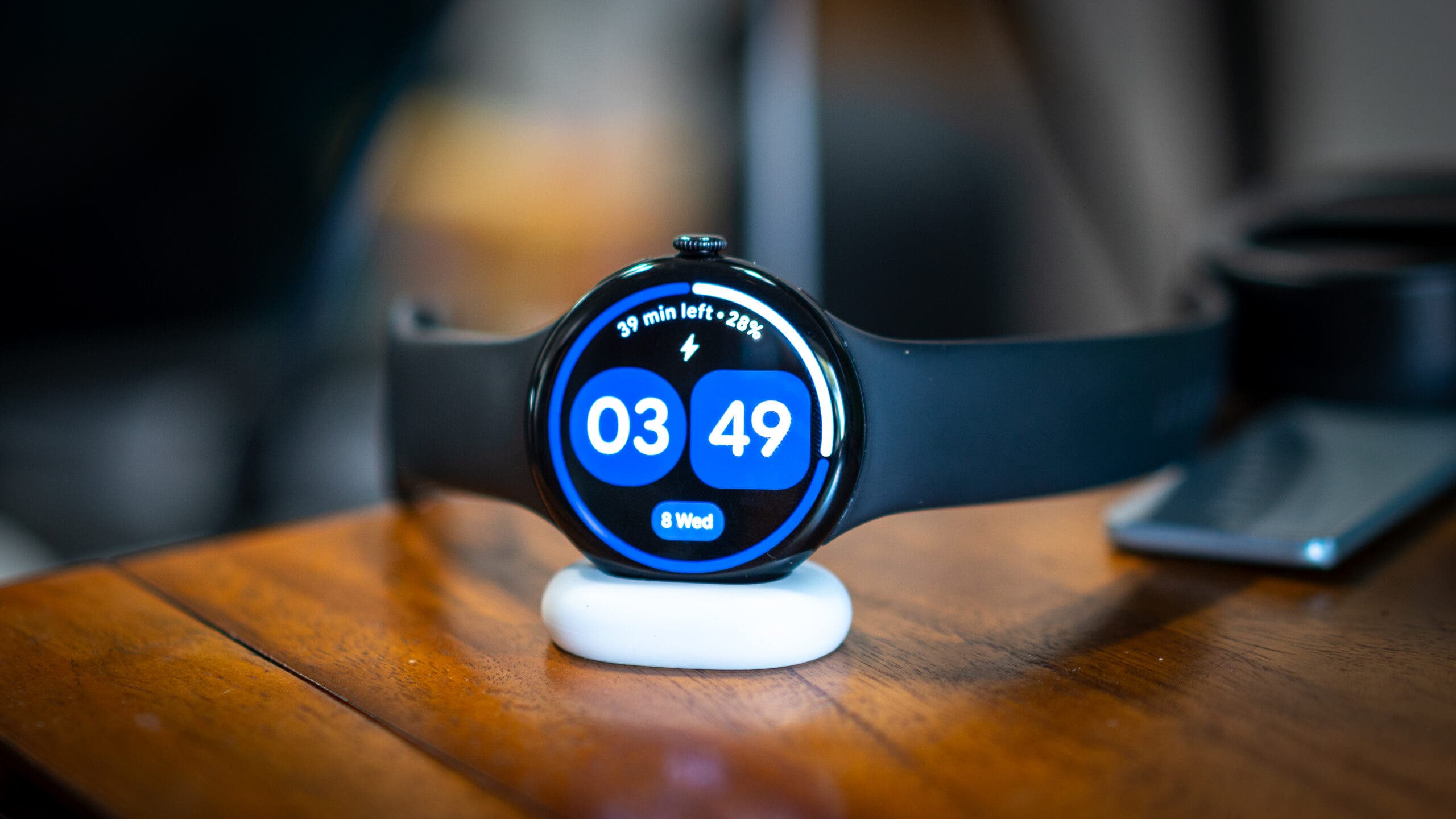 Google Pixel 4 watch displaying time in charging dock on wooden table