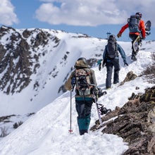 Snowboarders hiking snowy ridge towards mountain summit