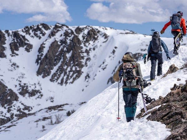 Snowboarders hiking snowy ridge towards mountain summit