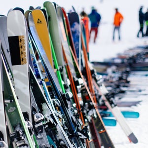 All-mountain skis lined up on ski rack at snowy base area during ski testing