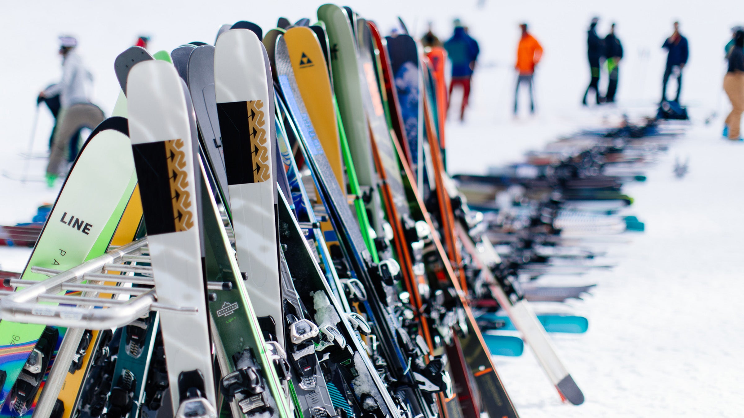 All-mountain skis lined up on ski rack at snowy base area during ski testing